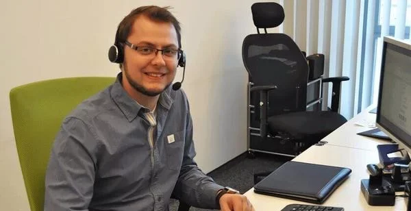 Ein Mitarbeiter spricht am Schreibtisch mit Headset und Computer, mitten in seiner Arbeit im Büro.