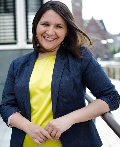 Eine Frau steht draußen vor Gebäuden und lacht - sie macht eine kurze Pause bei der Arbeit.