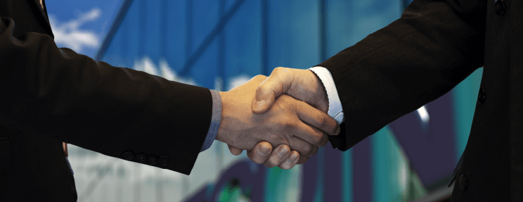 Zwei Menschen besprechen gemeinsam ein Projekt und reichen sich vor einem Bürogebäude die Hand.