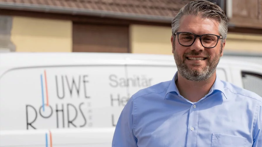 Ein Handwerker steht vor seinem Firmenwagen und bereitet sich auf den nächsten Einsatz vor.