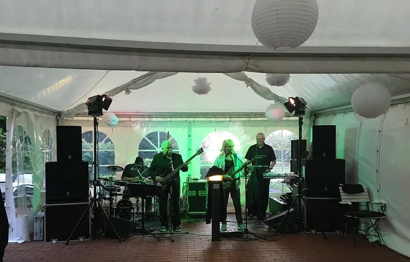 Mehrere Musiker spielen ihre Lieder auf einer Bühne im Zelt, umgeben von ihren Instrumenten und Lampions über den Köpfen.