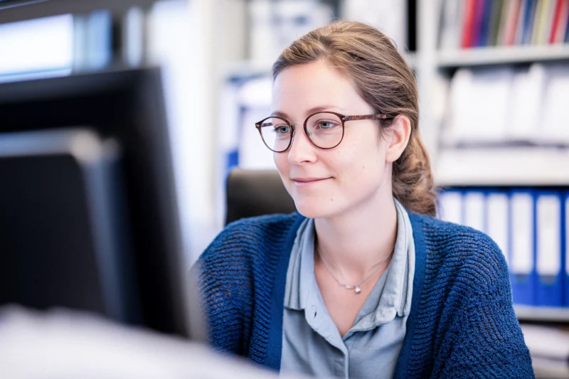 Eine Frau mit Brille, sitzt in einem Büro und arbeitet an ihrem Conputer.