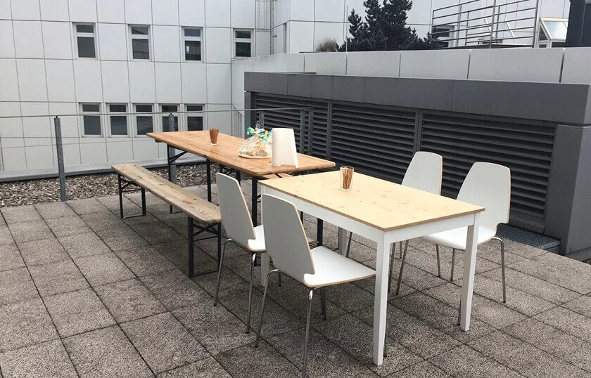 Zwei Hände decken Tische auf der Terrasse, stellen Blumen in eine Vase und bereiten die Sitzplätze für die Pause vor.